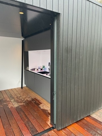 Black aluminum bifold glass doors fully opened connecting indoor living space to outdoor patio area