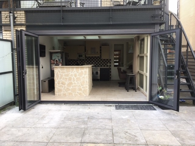 Black aluminum bifold glass doors fully opened connecting indoor living space to outdoor patio area