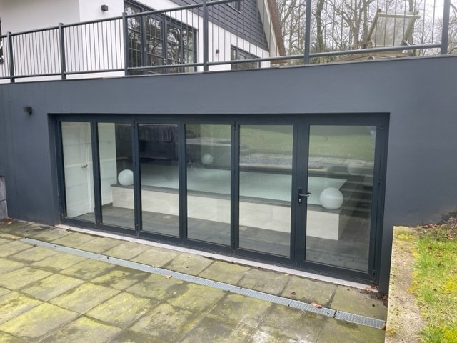 Black aluminum bifold glass doors fully opened connecting indoor living space to outdoor patio area