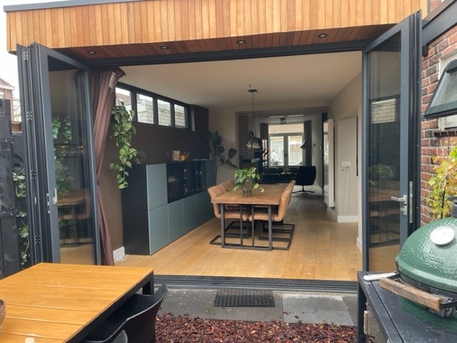 Black aluminum bifold glass doors fully opened connecting indoor living space to outdoor patio area