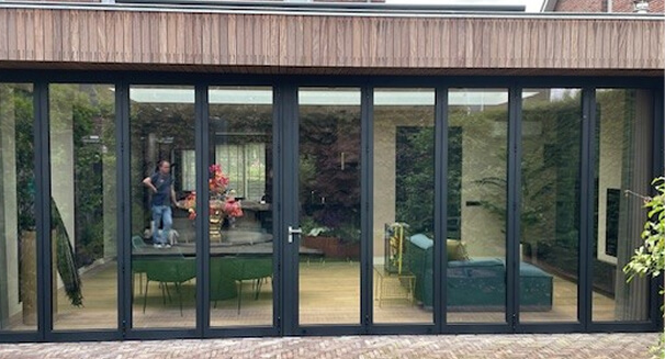 Large black framed sliding glass doors opening to modern interior living space with garden view