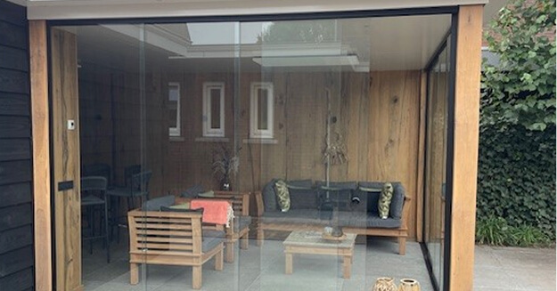 Sleek frameless glass sliding doors in wooden garden room extension with outdoor seating area