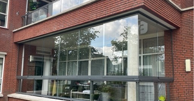 Modern glass extension with black aluminum frames on red brick residential building with balcony railings