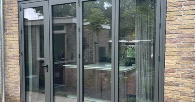 Contemporary grey aluminum bifold doors with glass panels installed in stone facade residential property