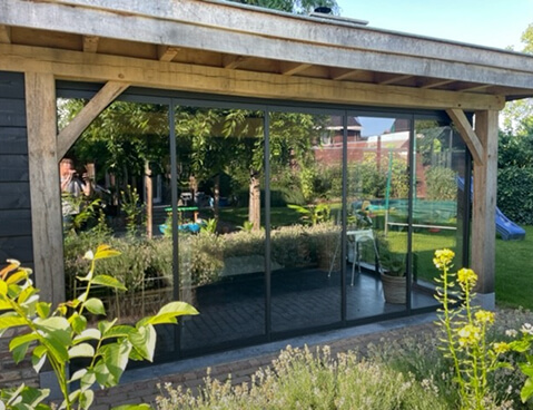 Frameless glass sliding doors installed in wooden garden pergola structure with natural landscape view